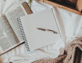 a journal on a bed with a blanket, tray, coffee