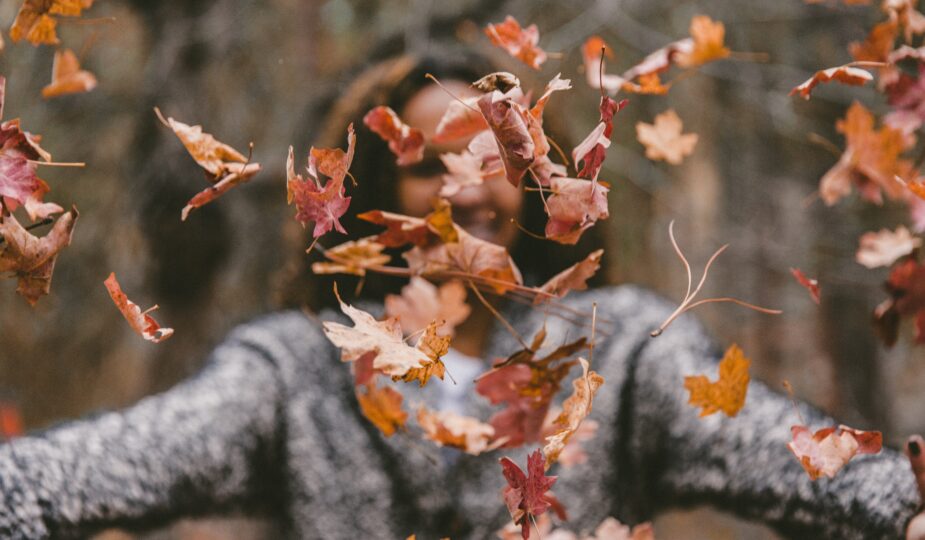 woman in a sweater throwing leaves