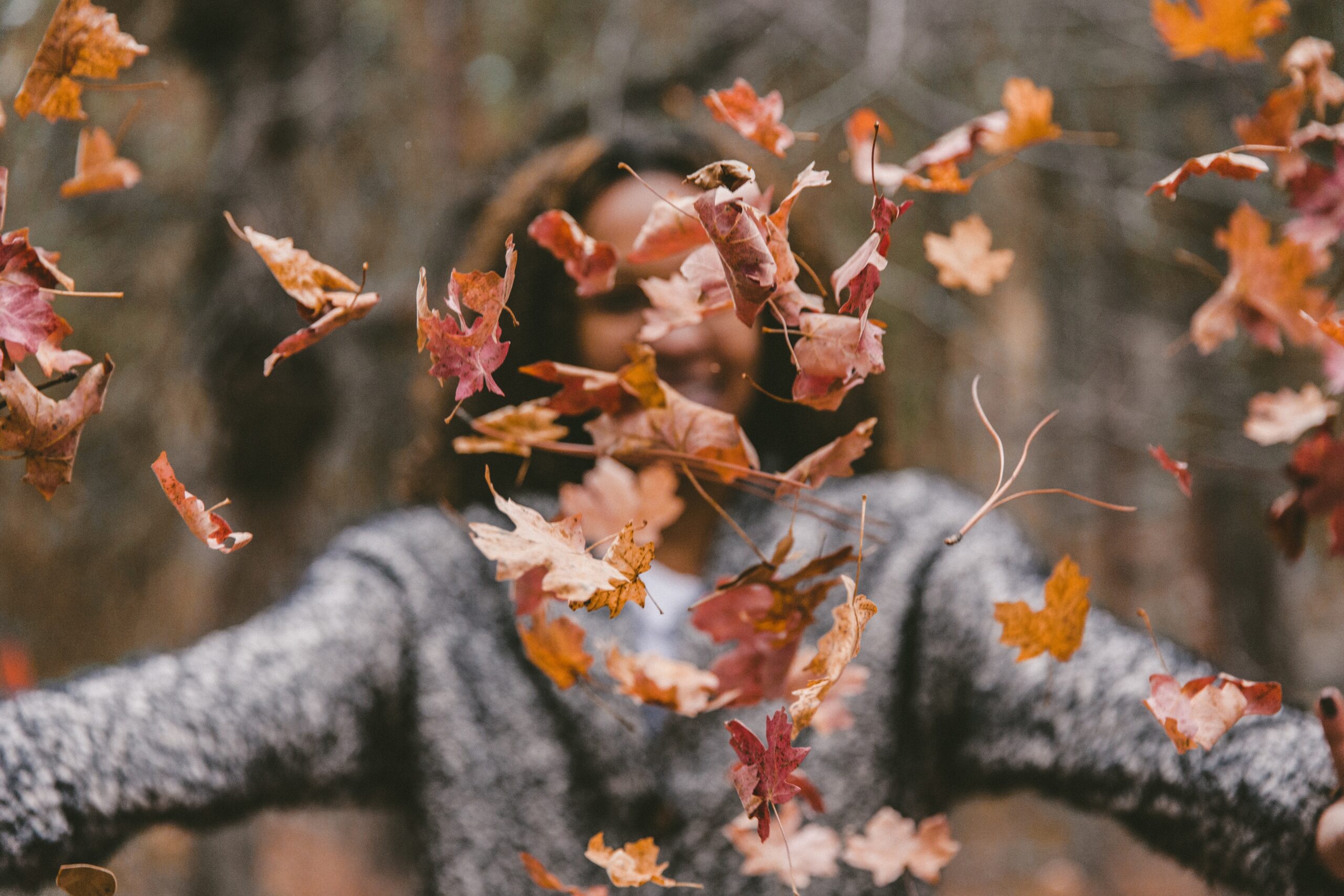 woman in a sweater throwing leaves